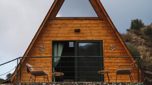 A wooden triangular cabin with a large sliding glass door, two chairs, and a small table on the front porch. - Scenic Mountain Getaway for Couples with Pool Access (Arakapas)