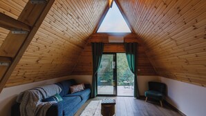 A cozy attic room with a sloped wooden ceiling, a sofa, a chair, and a small table. - Scenic Mountain Getaway for Couples with Pool Access (Arakapas)