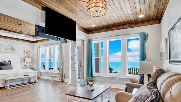 Una habitación amplia con cama, sofá, mesa de centro y vistas al mar a través de grandes ventanales.
