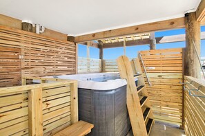A wooden spa area with a hot tub, wooden benches, and a pergola structure.