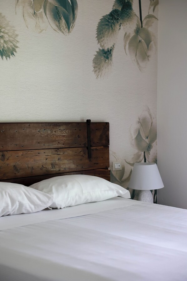 A bedroom with a wooden headboard, white bedding, and a wall-mounted lamp. - B&B Le GiAle (Castelnuovo del Garda)