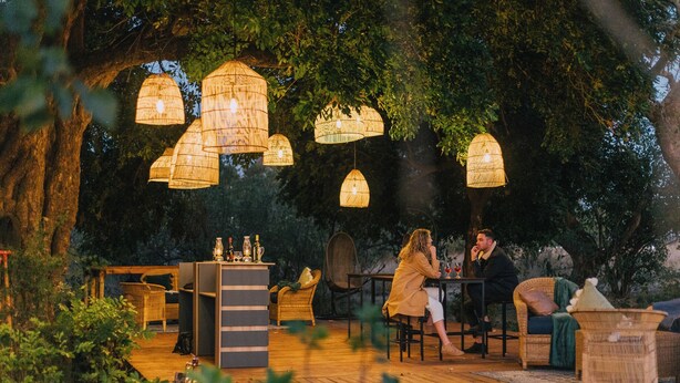 Een terras met rieten meubels, hanglampen en een houten terras.