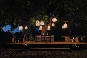 An outdoor seating area with wicker furniture and hanging lanterns under a large tree. - Kruger Untamed - Satara Plains Camp (MP)