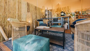 Een kamer met rieten meubels, een houten bijzettafeltje en een blauw, patroonrijk vloerkleed.