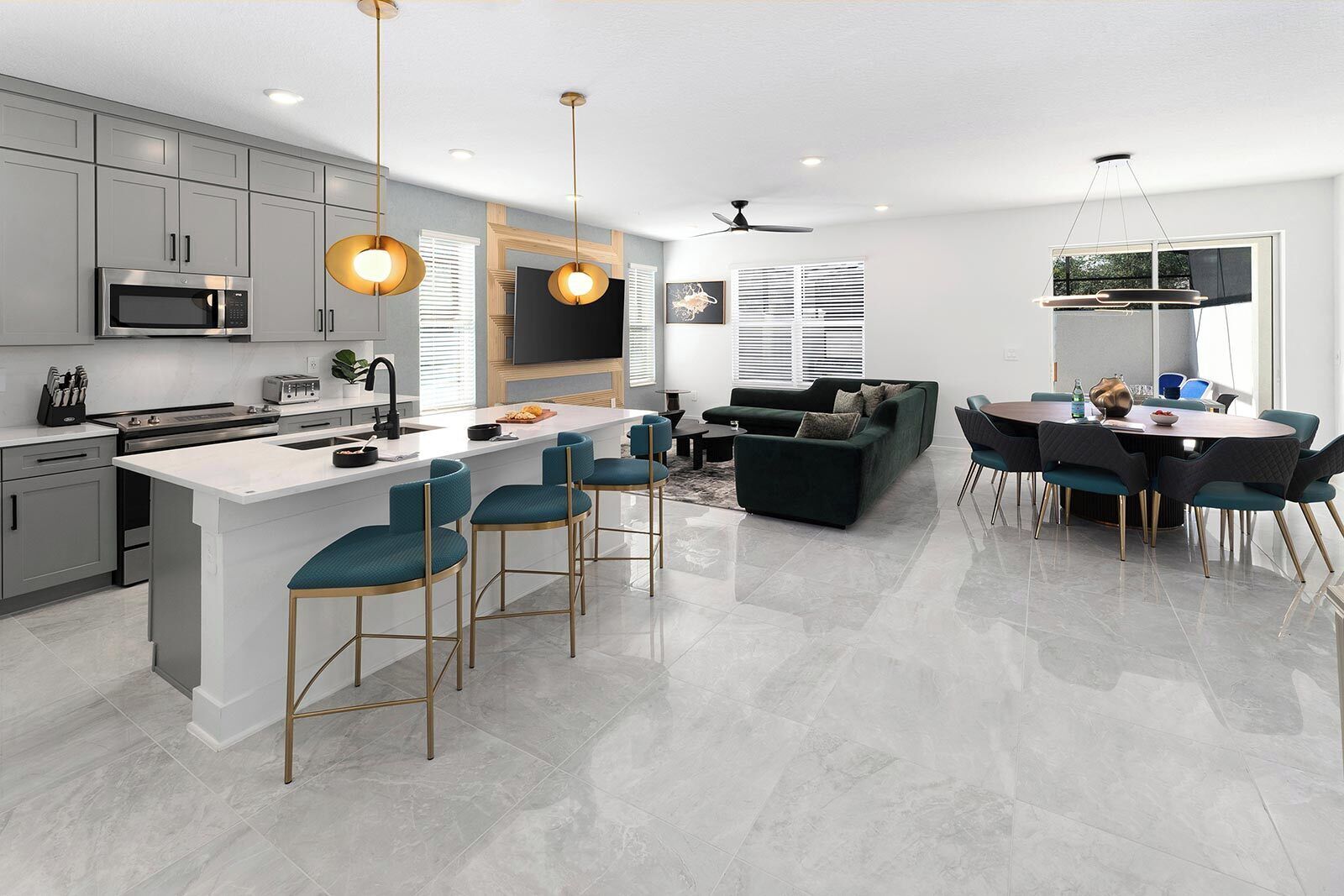 A modern kitchen with a central island, bar stools, a dining area with a round table and chairs, and a living area with a sofa and TV.