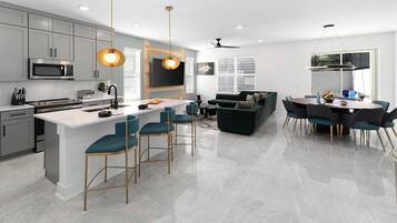 A modern kitchen with a central island, bar stools, a dining area with a round table and chairs, and a living area with a sofa and TV.