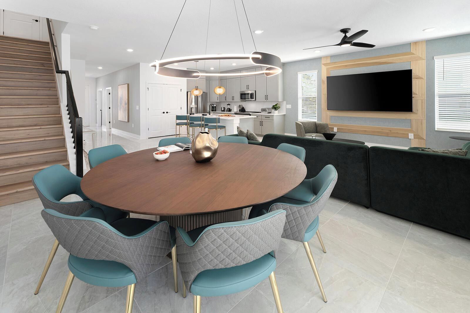 A modern dining area with a round table, teal chairs, and a central light fixture.