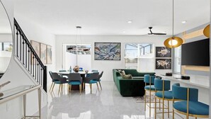 A modern living room with a dining area, a green sofa, and a TV on a stand. - Villa Marvelous | I-Drive Villa w/ Modern Decor, Luxe BRs, Huge LR/DR & PVT Pool (Orlando)