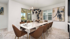 Un comedor moderno con piso de mármol, una mesa larga y sillas color café con patas doradas.