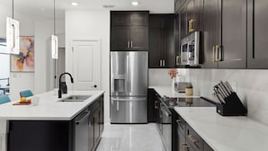 A modern kitchen with dark cabinets, stainless steel appliances, and a marble countertop.