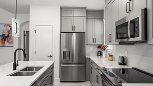 A modern kitchen with stainless steel appliances, white cabinetry, and a marble countertop.