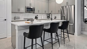 A modern kitchen with a central island, stainless steel appliances, and black bar stools.