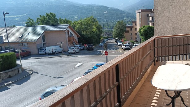 A balcony with a satellite dish, a view of a street with parked cars, and buildings in the background.