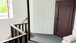 Une pièce avec une porte en bois sombre, un mur blanc, une fenêtre donnant sur un paysage verdoyant et un canapé blanc.