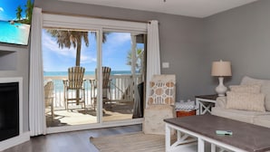 A living room with a television, a sofa, a coffee table, a lamp, and a view of the beach through a sliding door. - Direct Beach Access, Pet Friendly & Pool (Cape San Blas)