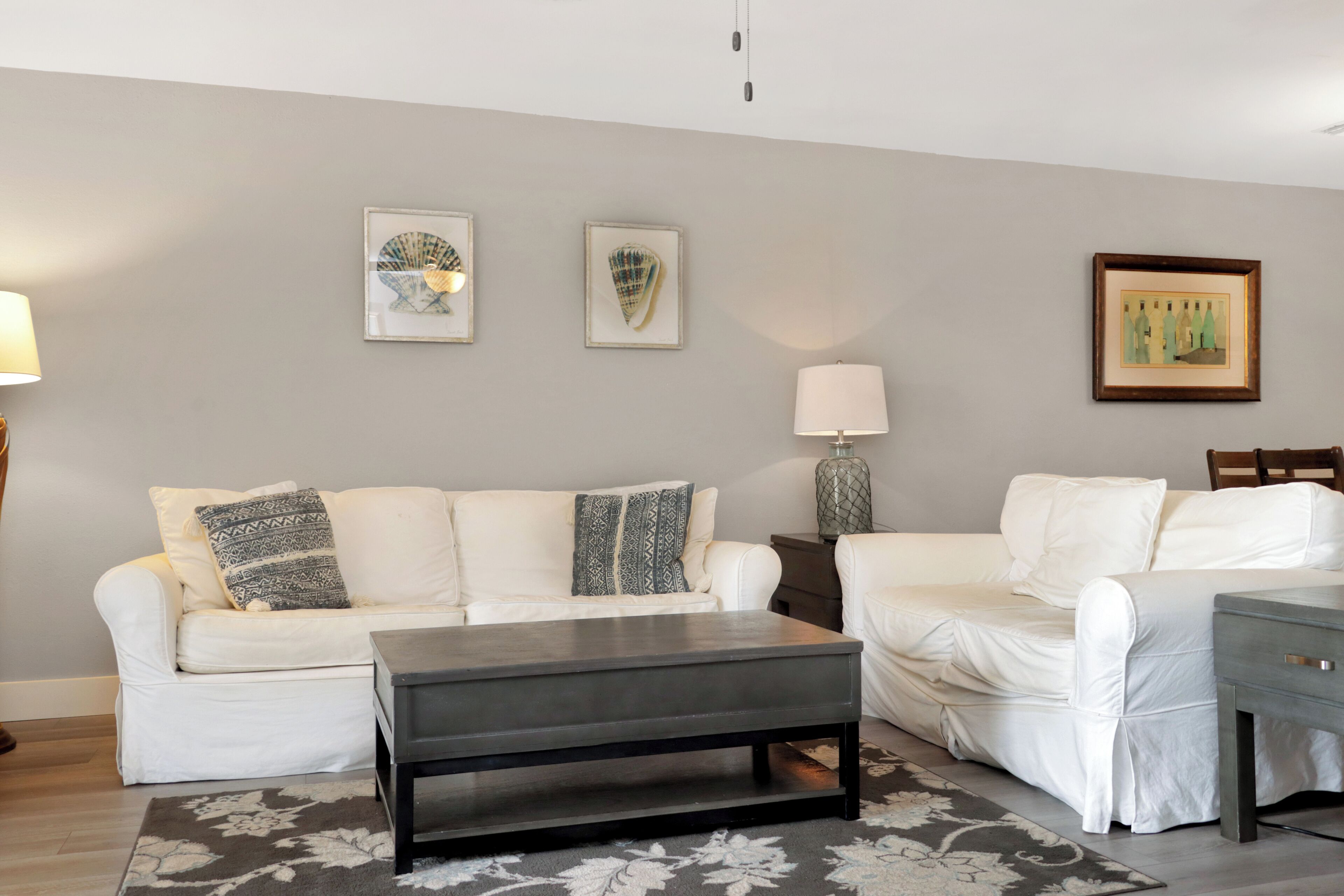 A living room with two white sofas, a dark coffee table, and a grey rug.