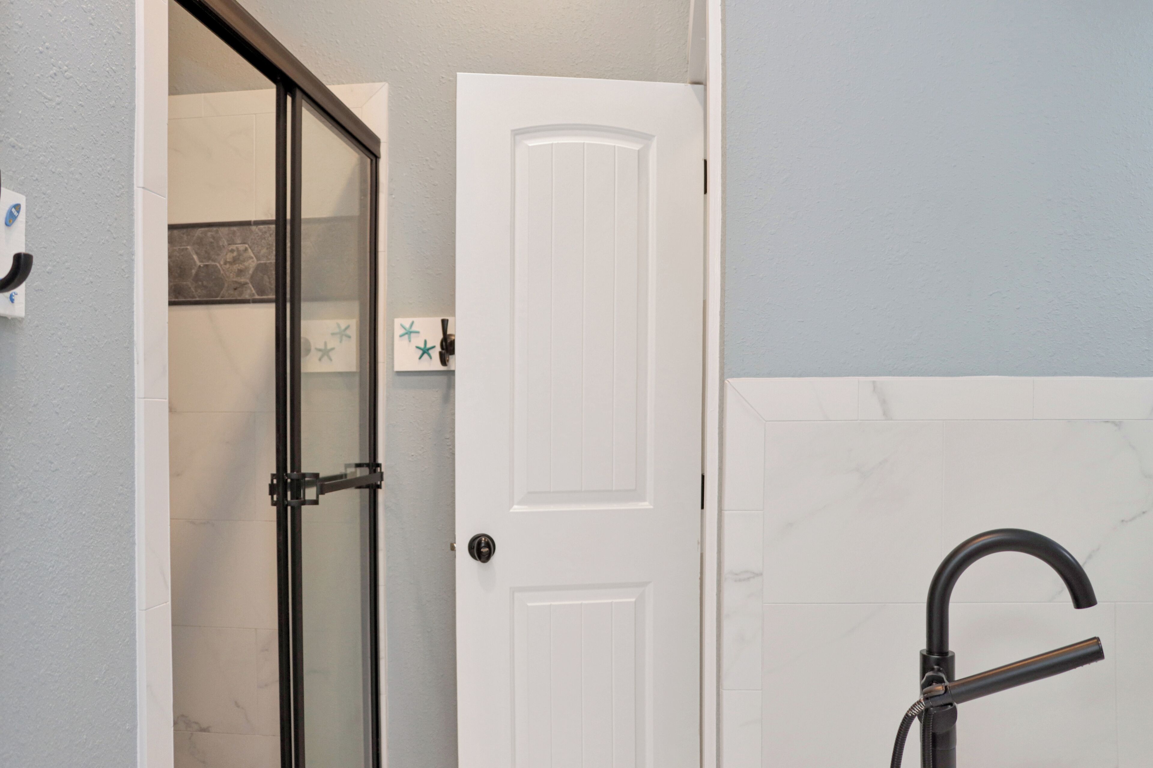 A bathroom with a glass shower door, a white door, and a black faucet.