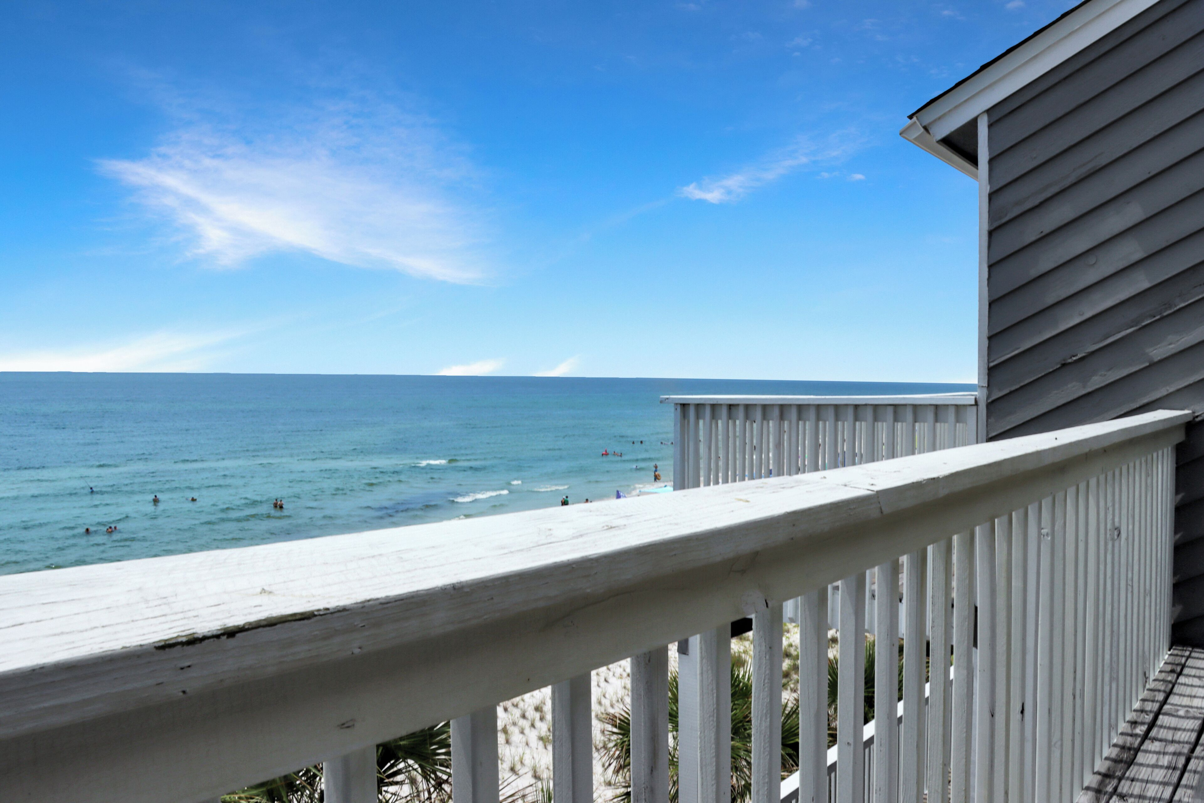 A wooden deck overlooking a beach with a clear view of the ocean and distant shoreline.