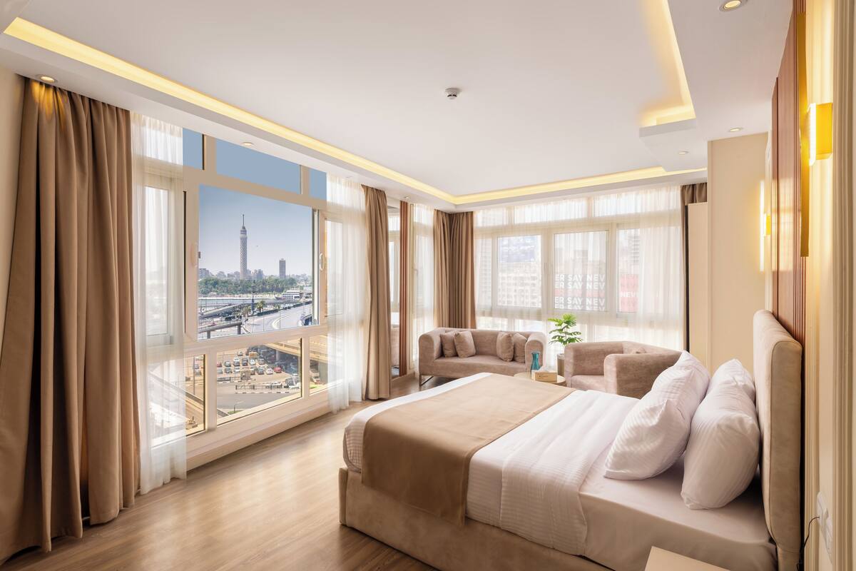 A modern hotel room with a large bed, a sofa, and a view of a cityscape.