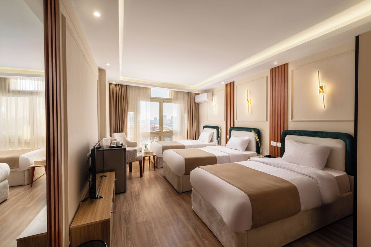 A hotel room with two beds, a desk, a chair, and a view of the city.
