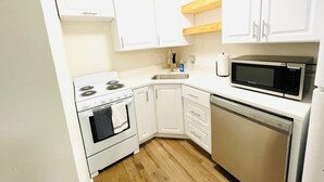 Een kleine keuken met witte kastjes, een fornuis, een magnetron en een vaatwasser.