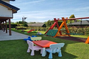 A children's play area with a swing set, slide, and a table with chairs.