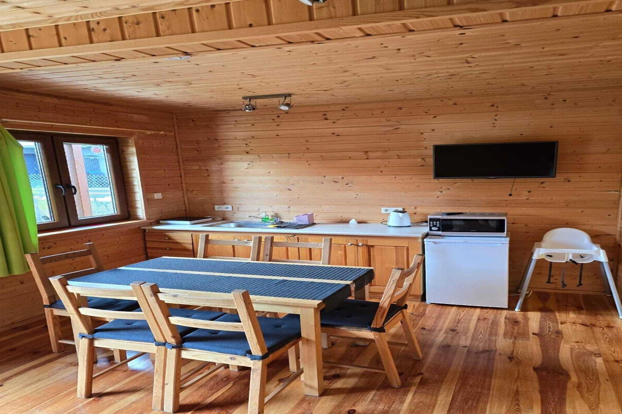 Un interno in legno con un tavolo da pranzo, sedie, un piccolo frigorifero, un forno a microonde e una TV a schermo piatto montata a parete.