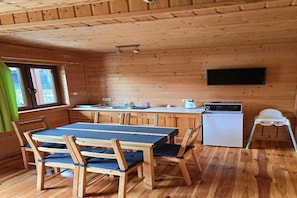 A wooden interior with a dining table, chairs, a small refrigerator, a microwave, and a flat-screen TV mounted on the wall.
