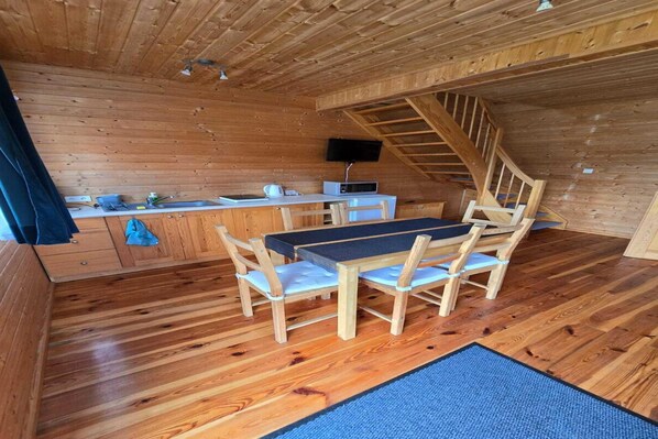 A wooden interior with a dining table, chairs, a kitchen area with a sink and microwave, and a staircase.