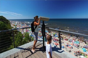 A person using binoculars overlooking a crowded beach with umbrellas and people.
