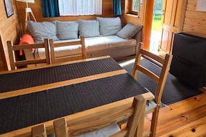Interior de una cabaña de madera con un sofá, una mesa de comedor y un televisor.
