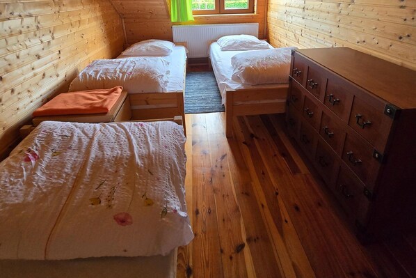 A cabin interior with two single beds, a wooden dresser, and a window with curtains.