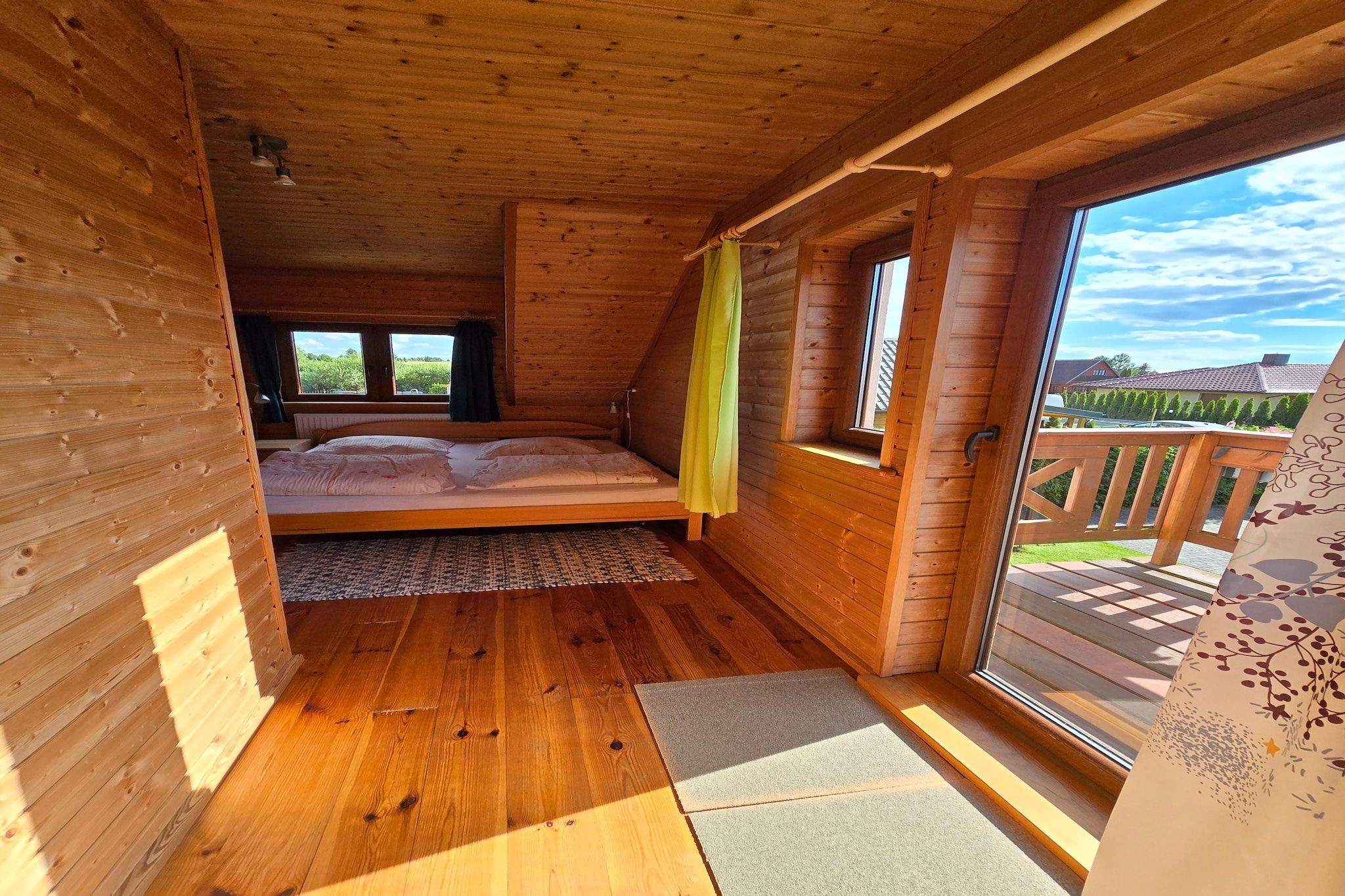 A wooden cabin room with a bed, a window, and a view of the outside.