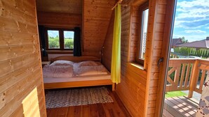 A wooden cabin bedroom with a bed, a window, and a view of the outside.