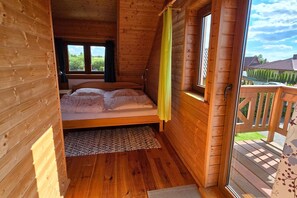 A wooden cabin bedroom with a bed, a window, and a view of the outside.