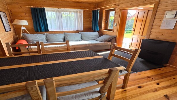 A wooden cabin interior with a sofa, table, chairs, and a fireplace.