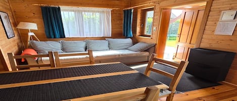 A wooden cabin interior with a sofa, table, chairs, and a fireplace.