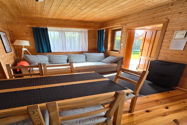 A wooden cabin interior with a sofa, table, chairs, and a fireplace.