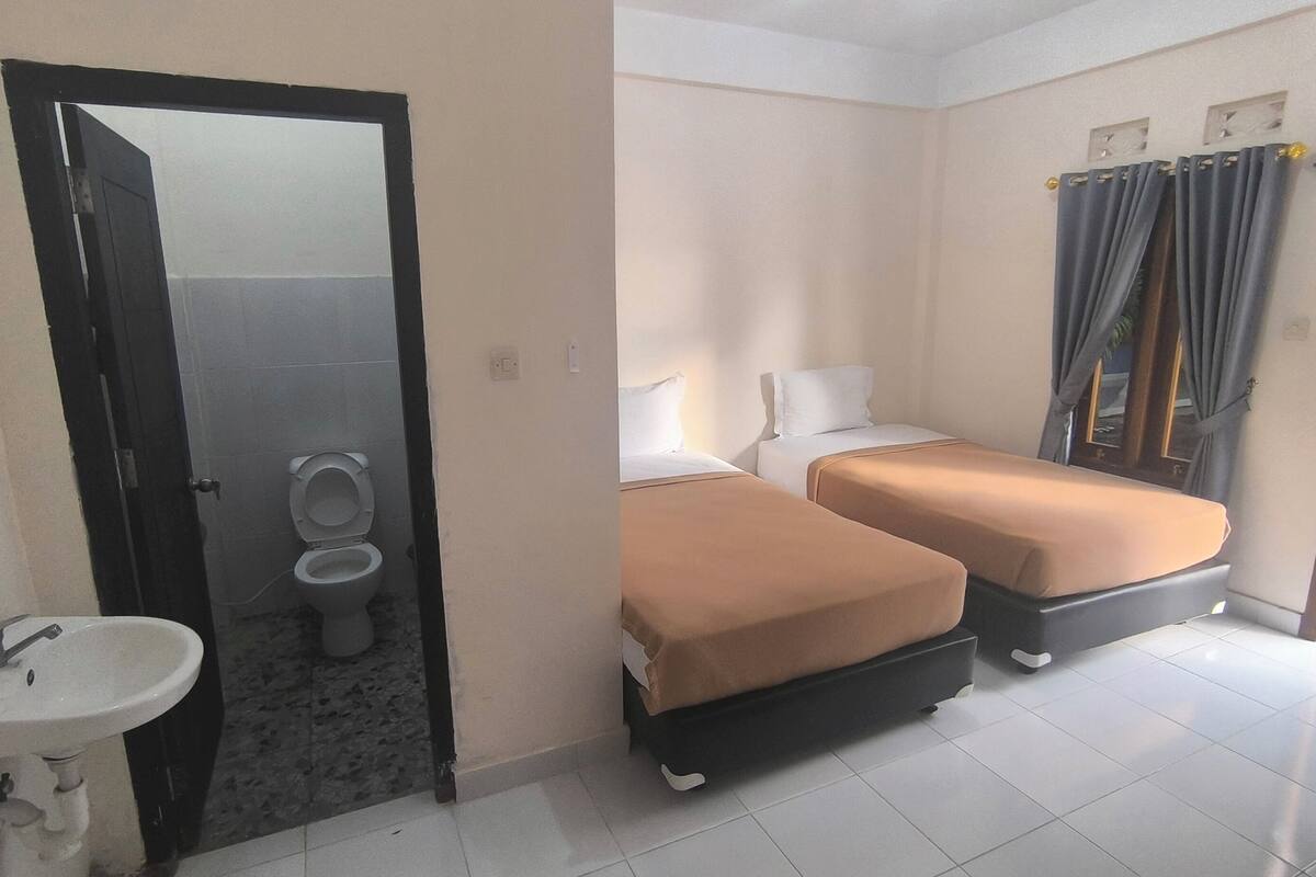 Una camera d'albergo con bagno, un lavandino, due letti e una finestra con tende.