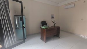 Een kamer met een houten bureau, een stoel, een potplant, een deur met een ruit en een airconditioning op de muur.