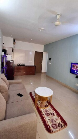 Una sala de estar con un sofá, una mesita redonda, un televisor y una zona de cocina al fondo.