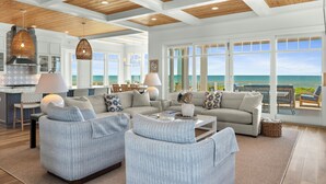 Un vaste espace de vie avec une grande fenêtre donnant sur l’océan, une cuisine équipée d’une cuisinière moderne et un coin salon confortable.
