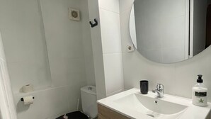Et badeværelse med toilet, vask, spejl og en lille skraldespand.