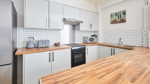 Une cuisine avec des meubles blancs, un plan de travail en bois, une cuisinière, un four à micro-ondes et un évier.