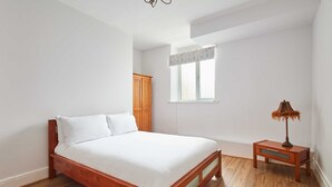 Une chambre à coucher avec un lit en bois, une table de chevet, une fenêtre avec des rideaux et une armoire.