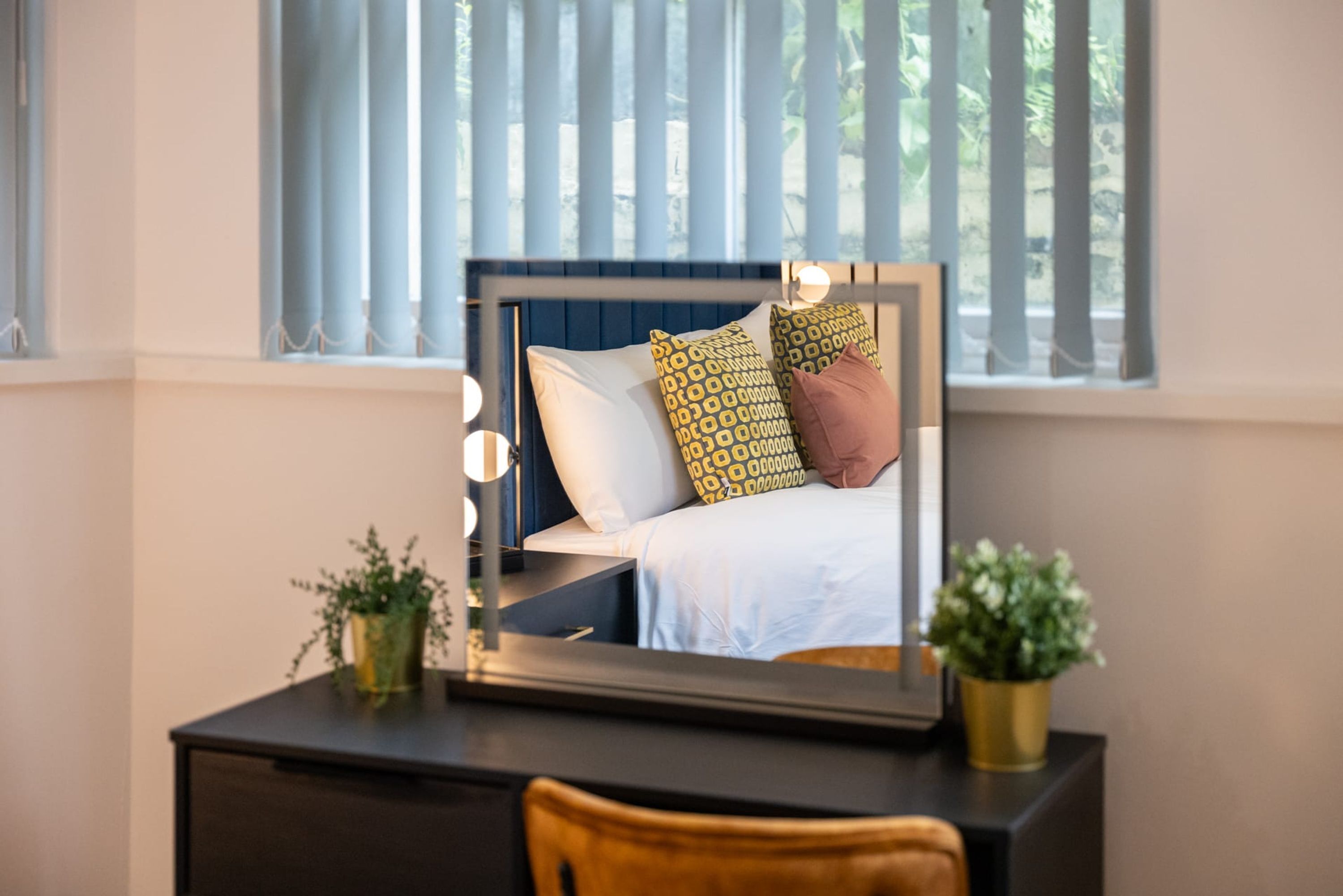 A bedroom with a bed, bedside table, and a mirror with lights.