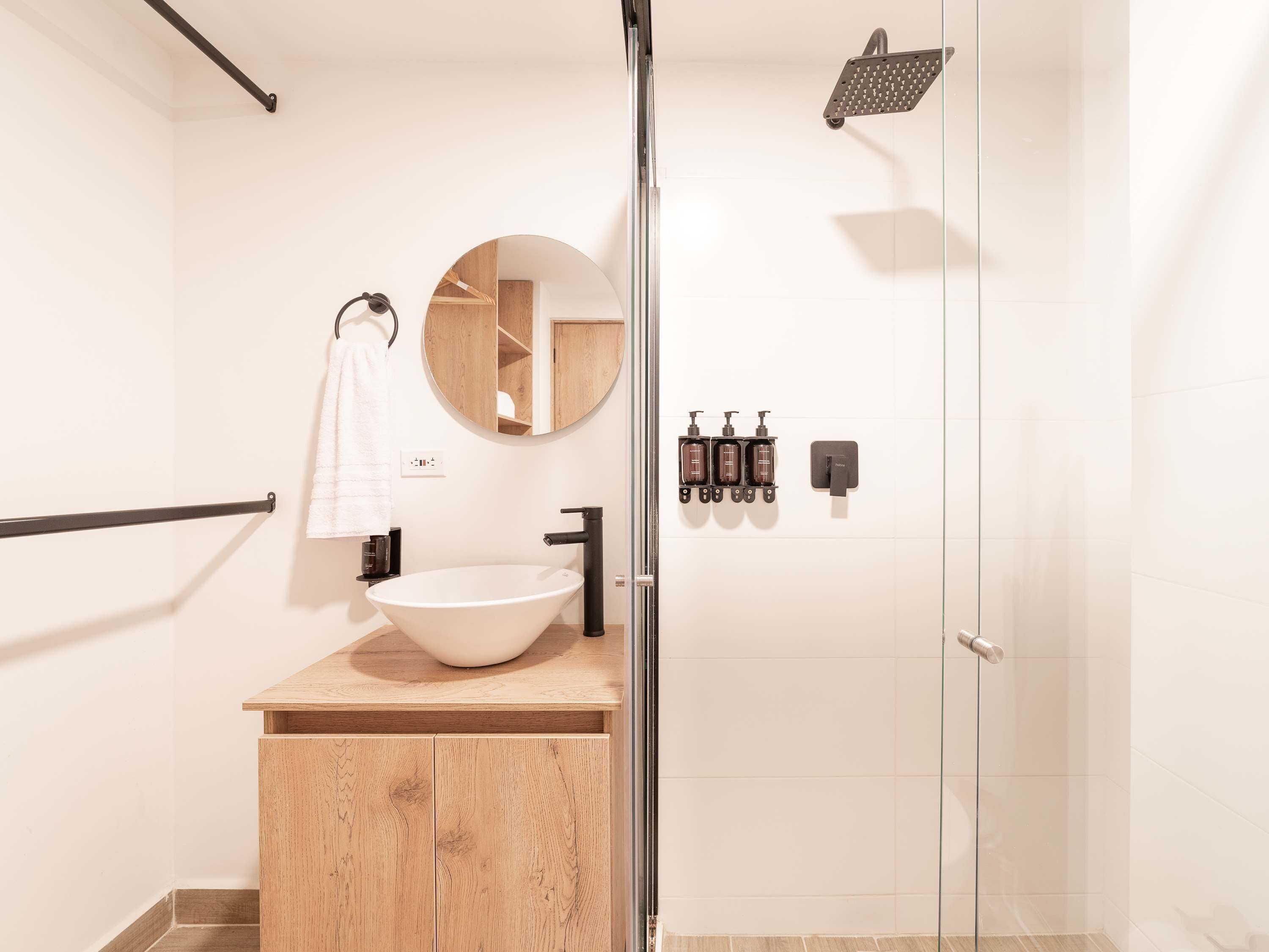 A modern bathroom with a freestanding sink, a round mirror, a glass shower enclosure, and a towel rack.