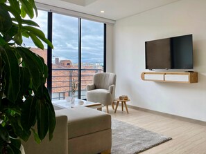 A modern living room with a large window, a sofa, a TV mounted on the wall, and a small side table. - w Majestic 2BR w Great View in Chapinero (Bogotá)