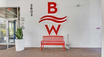 A building entrance with a red bench, a potted plant, and a fire alarm panel sign.