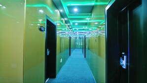 Un corridoio illuminato da luci al neon verdi e bianche, con pavimento rivestito di moquette e porte su entrambi i lati.